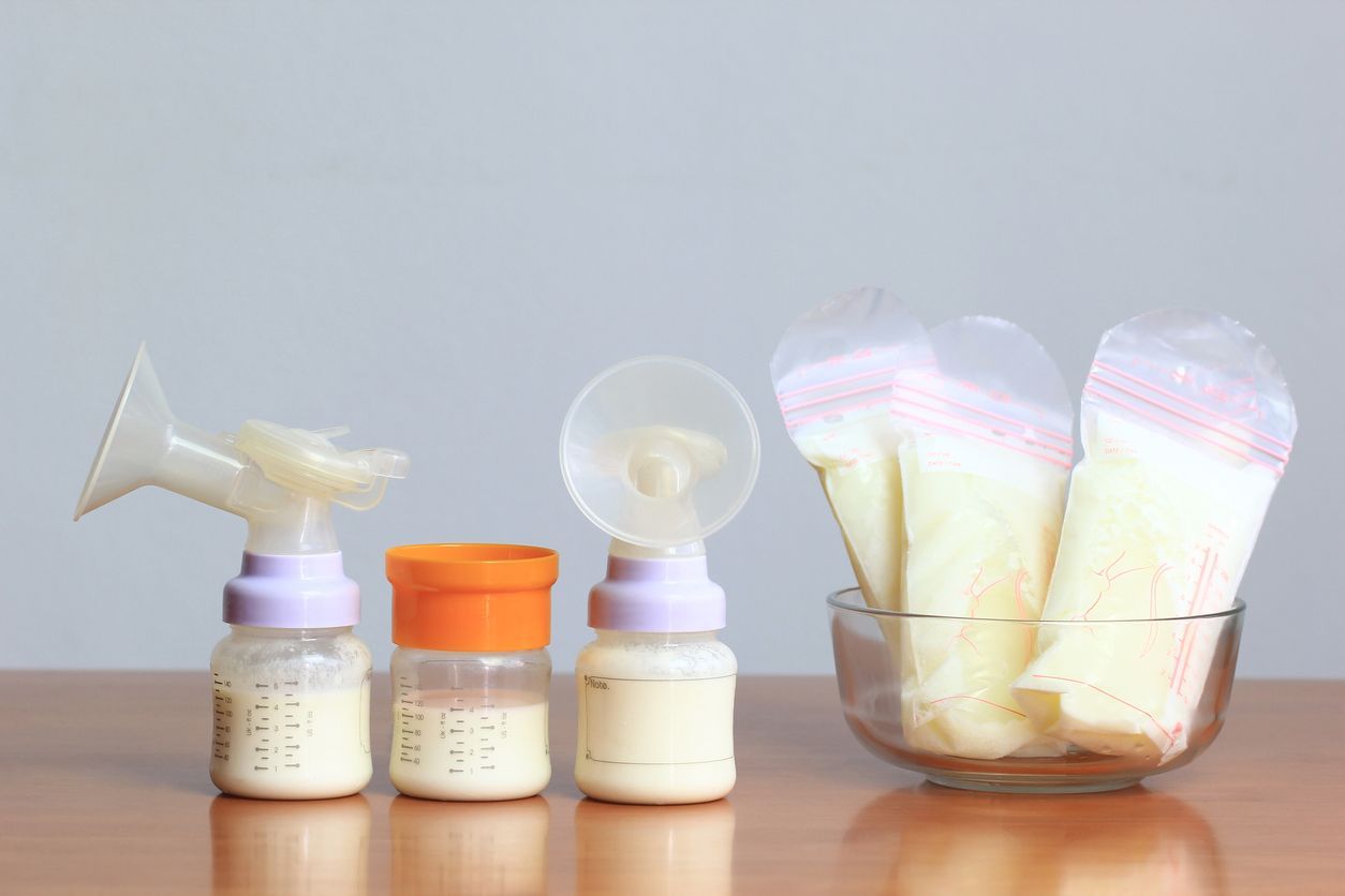 Manual breast pump and bottle with breast milk on the background of mother holding in her hands and breastfeeding baby. Maternity and baby care.