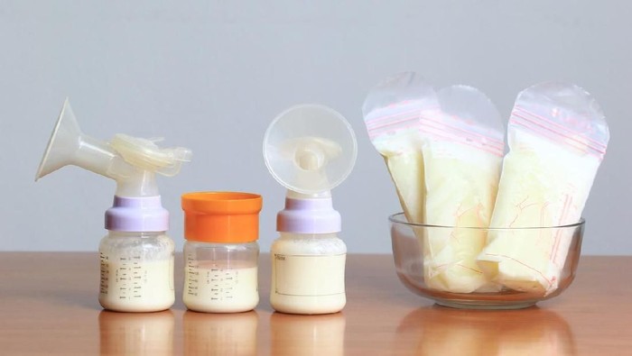 air susu ibu Manual breast pump and bottle with breast milk on the background of mother holding in her hands and breastfeeding baby. Maternity and baby care.