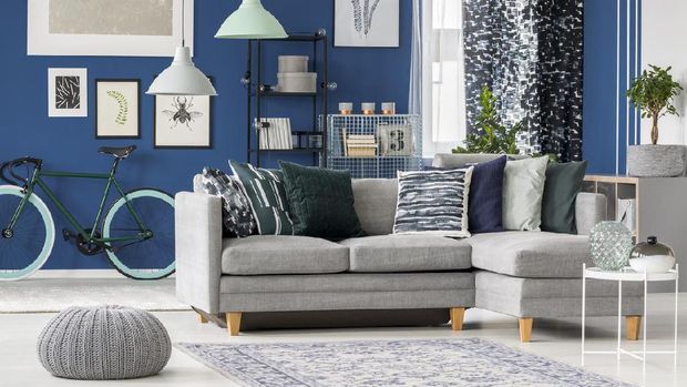 Cozy cushions and stylish textiles in a sunny, feminine living room interior with a pink, velvet sofa and a macrame on a white wall