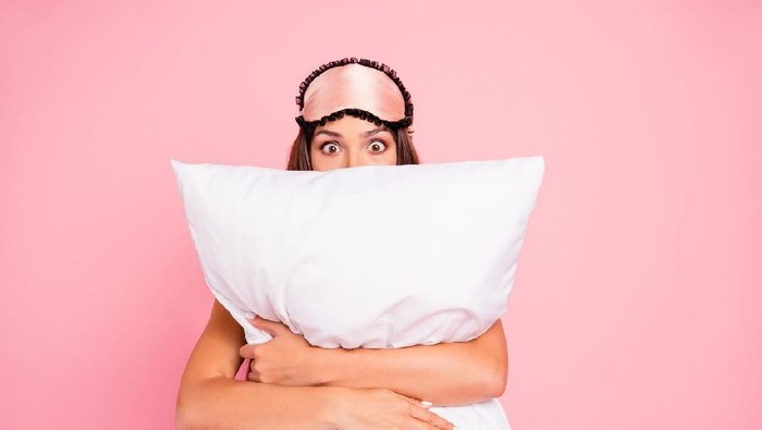 ilustrasi wanita tidur Young gorgeous shocked lady wearing eye mask, hugging pillow, hiding. Isolated over pink pastel background