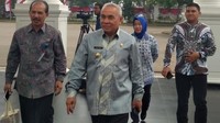 Isran mengenakan kemeja batik lengan panjang berwarna abu-abu bermotif dipadu celana panjang hitam.
