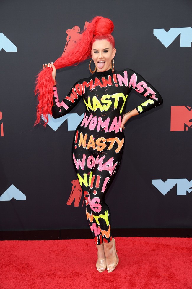 Justina Valentine menggunakan jumpsuit hitam dengan tulisan nasty woman penuh warna. Ditambah rambut merah dan anting jumbo, penampilannya tentu mencuri atensi siapa pun yang melihat. Foto: Dimitrios Kambouris/Getty Images