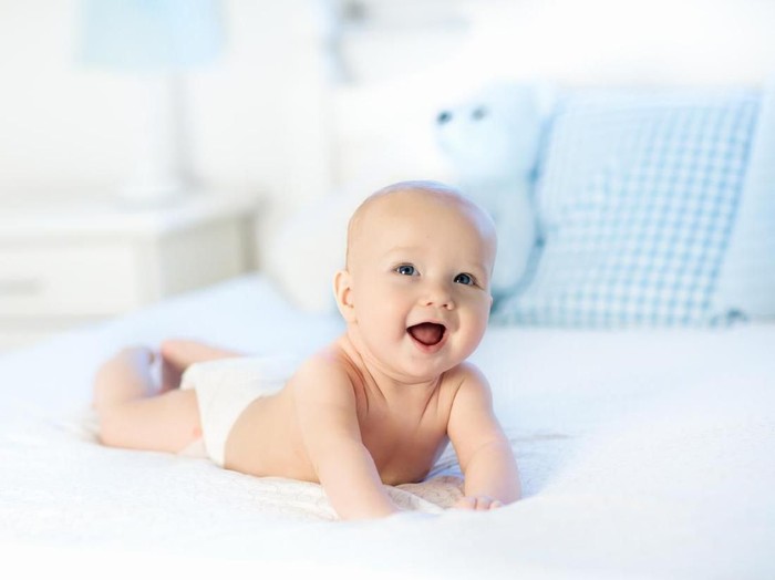 Ilustrasi bayi laki-laki Baby boy wearing diaper in white sunny bedroom. Newborn child relaxing in bed. Nursery for children. Textile and bedding for kids. Family morning at home. New born kid during tummy time with toy bear.
