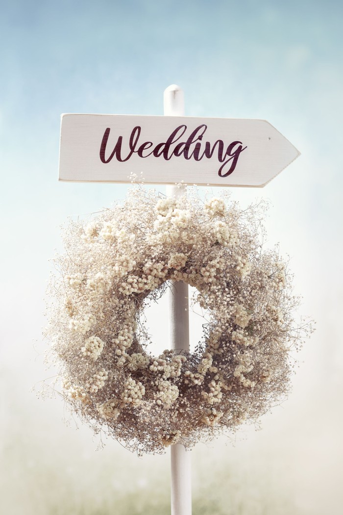 Rustic white wooden wedding directional sign and flower wreath in the garden.