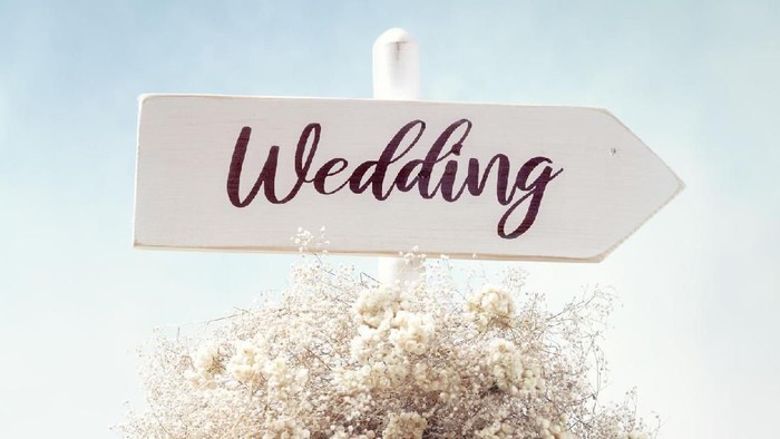Rustic white wooden wedding directional sign and flower wreath in the garden.