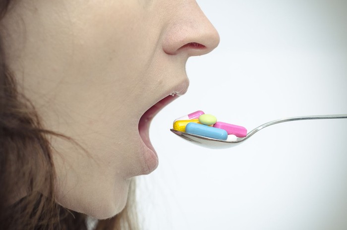 A woman opens her mouth for lots of colorful pills on a spoon.