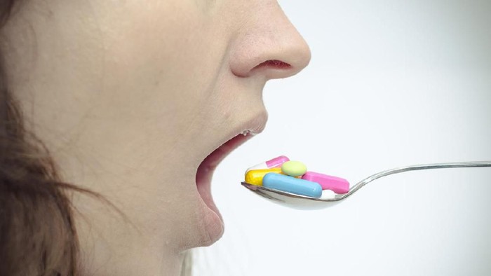 obat ilustrasi obat tablet pil kapsul A woman opens her mouth for lots of colorful pills on a spoon.