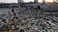 Seorang anak melintas di atas tumpukan sampah di sekitar permukiman warga.