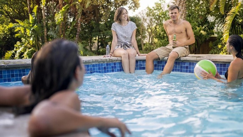 Ilustrasi Renang Topless Female friends talking while sitting at poolside. Women are swimming in water. They are enjoying during summer vacation.