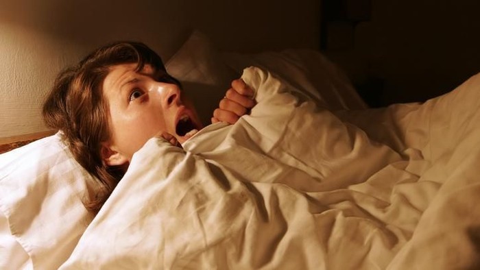 A woman in the bed in the dark expressing fear