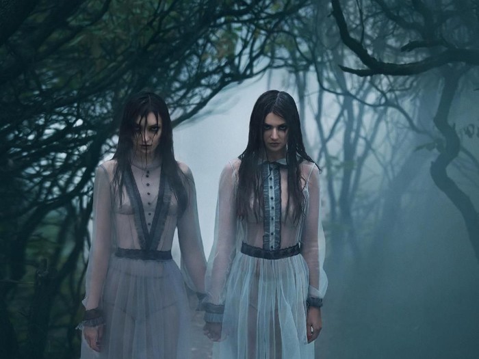 The girls are crying. Young ladies in ancient dresses walking through the woods in search of a victim. Foggy, spooky forest. Photoshoot in the style of horror. Mystical photo. Fashionable tinted.Creative color.