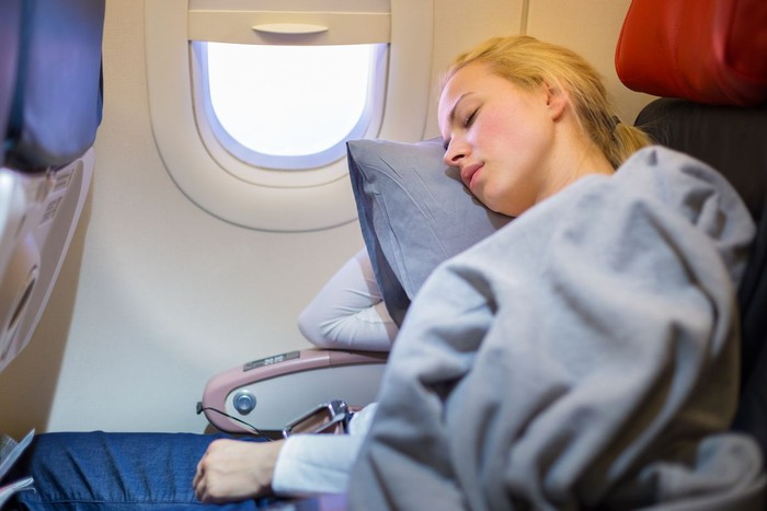 Female passenger sleeping covered with blanket. Comfortable flying.