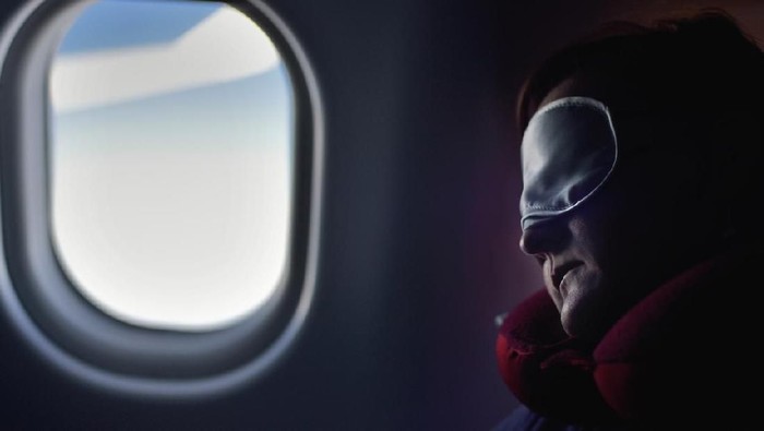 Female passenger sleeping covered with blanket. Comfortable flying.