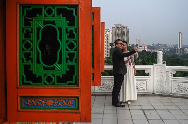 Pasangan pengantin yang baru saja mengikuti nikah massal di tanggal cantik 9-9-2019, berpose selfie di Thean Hou Temple. Lokasi pernikahan ini juga dikenal sebagai tempat wisata yang Instagramable. Foto: Mohd RASFAN / AFP