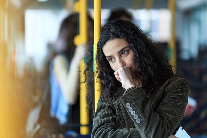 Pensive young woman traveling with bus and holding smart phone. Wears casual clothes.