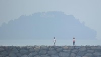 Di Padang Sumatera Barat pun ikut terimbas dari Karhutla. Warga berolahraga dengan latar Gunung Padang yang diselimuti kabut asap di Pantai Padang, Padang, Sumatera Barat, pada Kamis (12/9/2019). Foto: ANTARA FOTO/Iggoy el Fitra