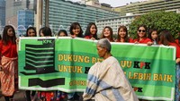 Seorang pemulung melintas di depan para wanita yang membentangkan spanduk tersebut.