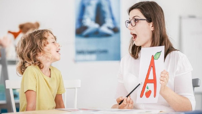 Speech therapist working with a child on a correct pronunciation using a prop with a letter a picture.