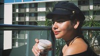 Dengan memakai baju serba hitam lengkap dengan topi modisnya, Sahila berpose sambil memegang segelas kopi saat pagi hari. Foto: Instagram @sahilahisyam