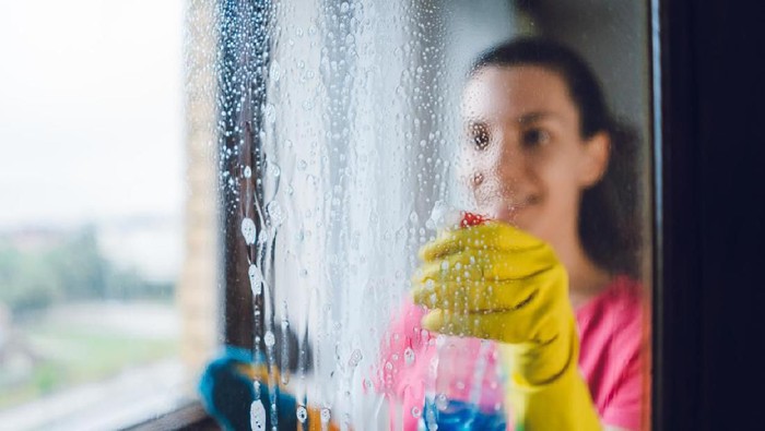 Young woman wiping windows at home