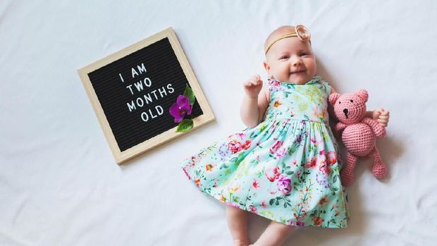 Adorable two month old baby girl wearing floral dress and headband. Shot from overhead on white background.