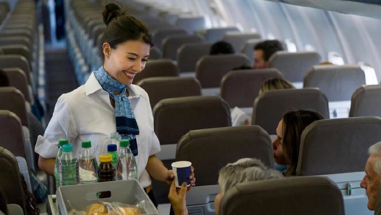 Portrait of a friendly flight attendant serving food and drinks in an airplane and looking happy - travel concepts