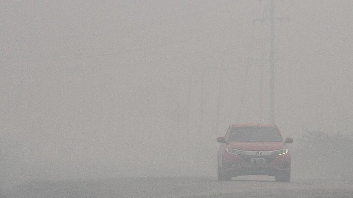 Pengendara kendaraan bermotor menembus kabut asap pekat ketika terjadi kebakaran lahan di Kabupaten Pelalawan, Riau, Kamis (19/9/2019). Kebakaran lahan yang terjadi di tepi jalan koridor ini membuat pengendara kendaraan bermotor harus ekstra hati-hati karena terbatasnya jarak pandang di kawasan tersebut.