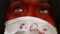 Seorang peserta aksi peduli iklim di Brasil mengenakan masker bertuliskan SOS sebagai simbol dampak kerusakan hutan Amazon. Istimewa/Eraldo Peres/AP Photo.