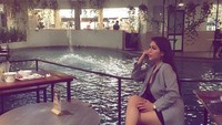 Foto ini diambil secara candid, memperlihatkan Gebby memakai celana pendek yang sedang duduk di sebuah restoran dengan pemandangan kolam renang. Foto: Instagram @gebby.vesta_