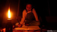 Seorang anak tengah mengerjakan pekerjaan rumah diterangi dengan cahaya lilin saat pemadaman listrik bergilir terjadi di wilayah Simeulue, Aceh.