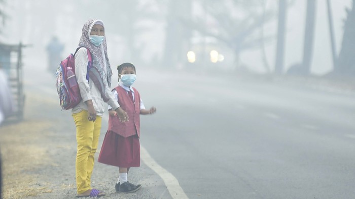 Seorang siswa bersama orang tuanya mengenakan masker  saat menunggu angkutan umum, di Palembang, Sumatera Selatan, Senin (23/9/2019). Pemerintah Kota Palembang meliburkan siswa sekolah selama tiga hari, 23-25 September 2019 akibat asap yang dapat membahayakan kesehatan. ANTARA FOTO/Mushaful Imam/wpa/ama.
