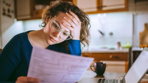 Young brunette curly female reading her bill papers, looking stressed
