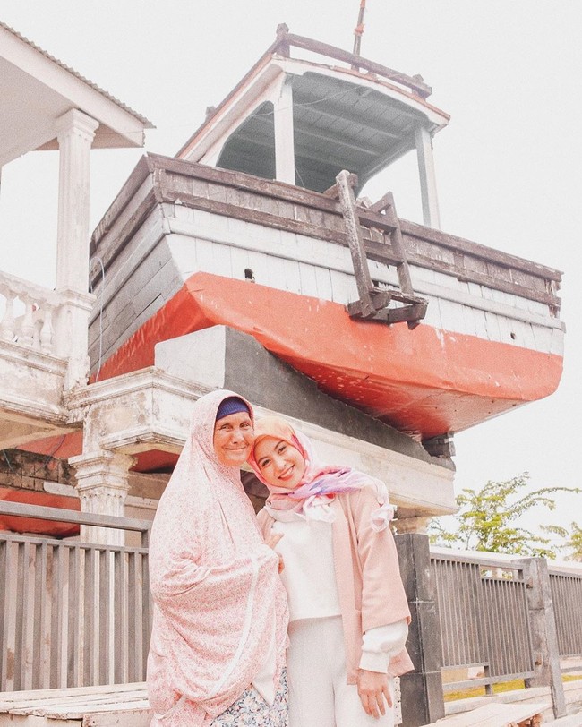 Tampil dengan hijab motif dan busana serba pastel, Awkarin berpose dengan seorang ibu asli Aceh yang pernah mengalami bencana Tsunami. Keduanya berpose di kawasan wisata Kapal di Atas Rumah. Foto: Dok. Instagram @awkarin