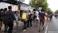 Para mahasiswa duduk-duduk di pinggir jalan sambil menunggu kedatangan dua bus pengganti.