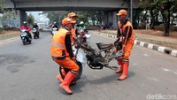 Tiga orang petugas nampak menggotong bangkai motor ke pinggir jalan agar tak mengganggu lalu lintas di jalan.