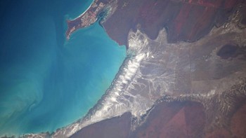 Pemandangan lautan biru dan daratan yang unik dengan lanskap daratan yang gersang kecoklatan (Christina Koch/Twitter)