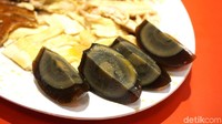 Satu telur pitan berwarna kehiataman ini dibagi menjadi empat, dan disajikan bersama menu ayam kampung. Tekstur telurmya kenyal, lebih mirip seperti agar-agar atau jelly yang kenyal, dan kuning telur yang sudah menghitam rasanya jauh lebih gurih dan creamy. Tak ada aroma amis sama sekali karena irisan jahe yang tersedia di piring. Foto: dok. detikFood