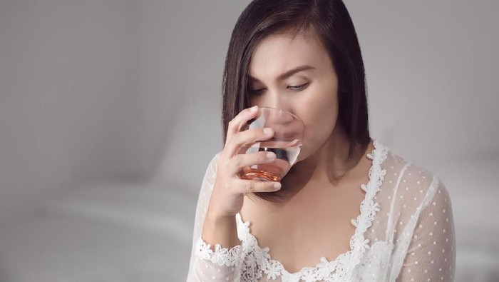 Asian woman in white nightwear drinking water before bedtime for good health at bedroom. Basic concepts in health and health care.