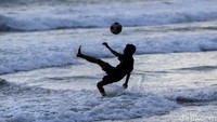 Seorang anak menunjukkan keahliannya mengolah bola di pinggir pantai kala matahari perlahan-lahan mulai terbenam.