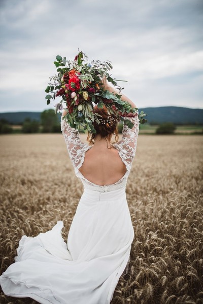 Stunning young bride with bouquet of wedding flowers standing in the wheat field