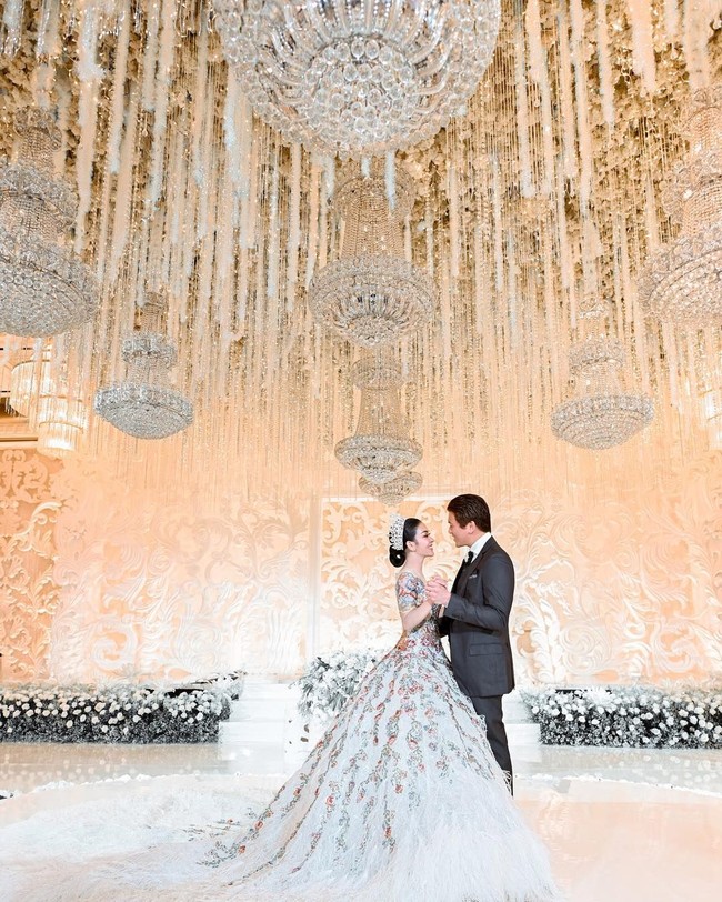 Syahrini dan Reino Barack memilih dekorasi pernikahan mewah serba putih untuk resepsi pernikahan kedua mereka yang digelar di Hotel Four Seasons, Jakarta. Lampu chandelier dan bunga-bunga yang menjuntai serta tirai manik-manik berwarna putih mengukuhkan kesan mewah di pernikahan Syahrini dan Reino. Foto: Instagram