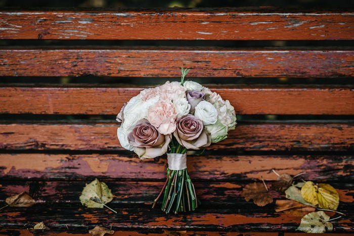 The wedding bouquet of the bride is on a bench with yellow autumn leaves in the park. Bouquet of pale pink, white and brown flowers.