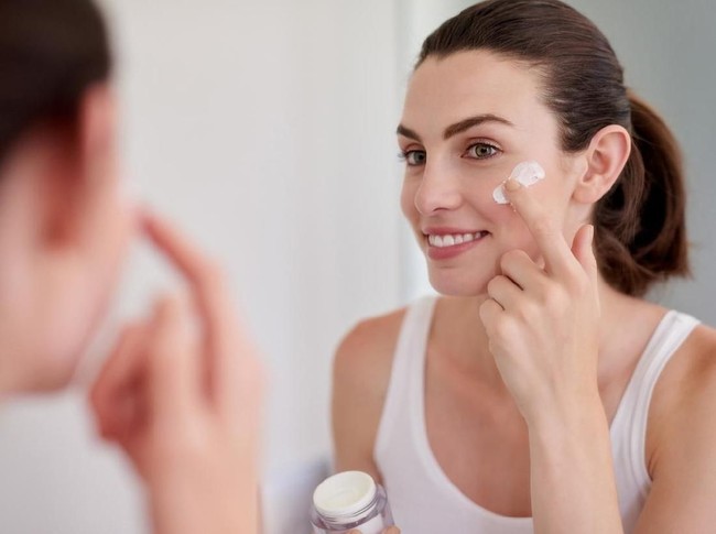 Shot of an attractive young woman applying moisturiser in front of a bathroom mirror