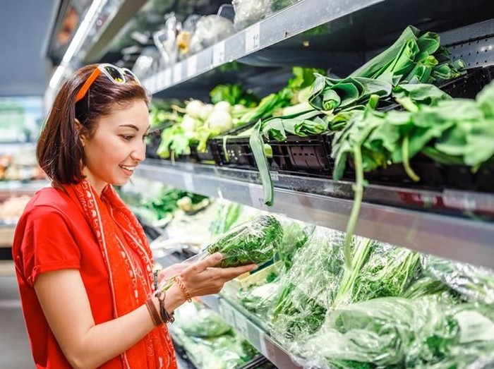 sayuran hijau Woman with cart shopping in grocery store in the produce section. Using smart phone