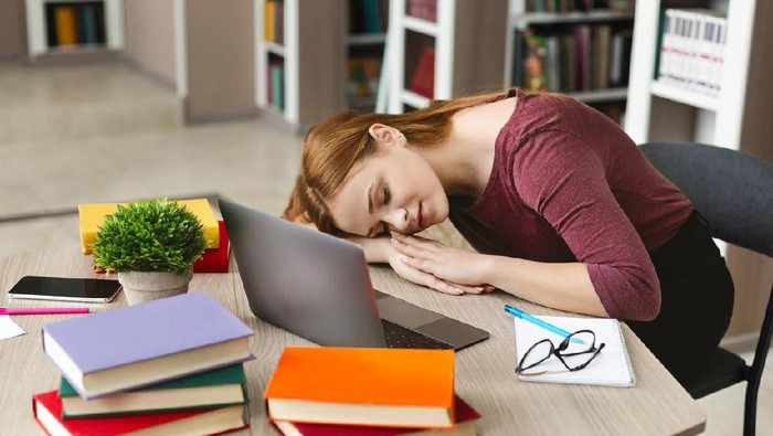 Exhausted caucasian girl having nap in front of laptop, studying at library, copy space