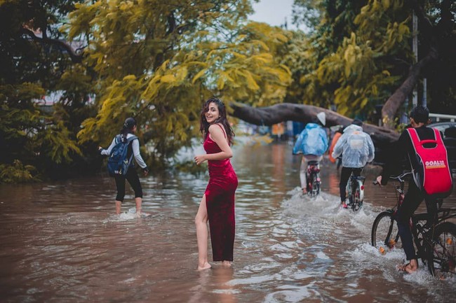 Warga lain yang berusaha menerjang banjir dijadikan sebagai latar belakang foto. Sementara wanita tersebut berpose dengan wajah tersenyum. Foto: Instagram/@meowwala
