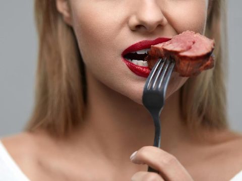 Woman Eating Meat. Closeup of Healthy Hungry Girl With Beautiful Face, Red Lips Eats Delicious Grilled Meat. Female Mouth Biting Piece Of Tasty Beef Steak On Fork. Nutrition Concept. High Resolution