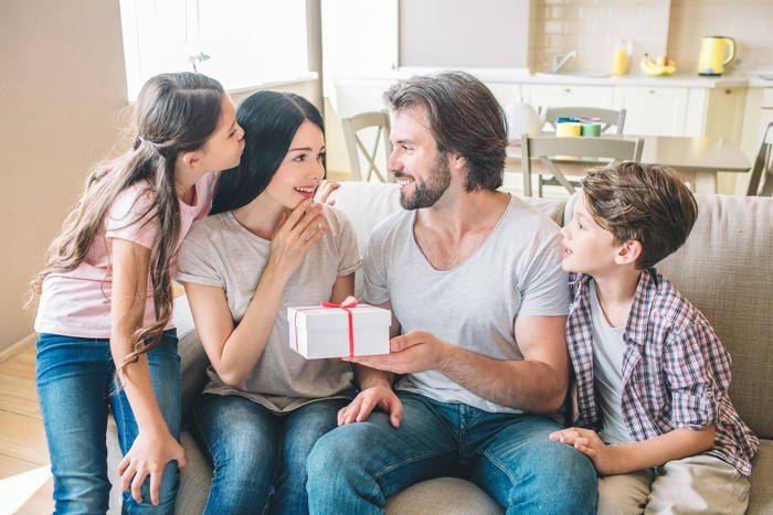 zodiak Amazed woman looks at present that man holds. She is surprised and happy. Kids look at parents