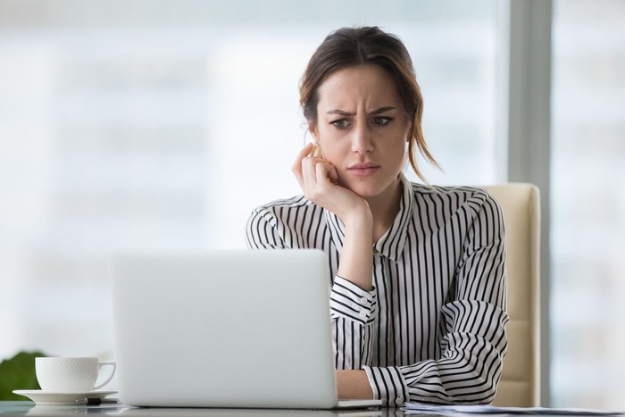 Confused businesswoman annoyed by online problem, spam email or fake internet news looking at laptop, female office worker feeling shocked about stuck computer, bewildered by scam message or virus