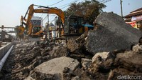 Alat berat menghancurkan bahu jalan untuk dijadikan trotoar.